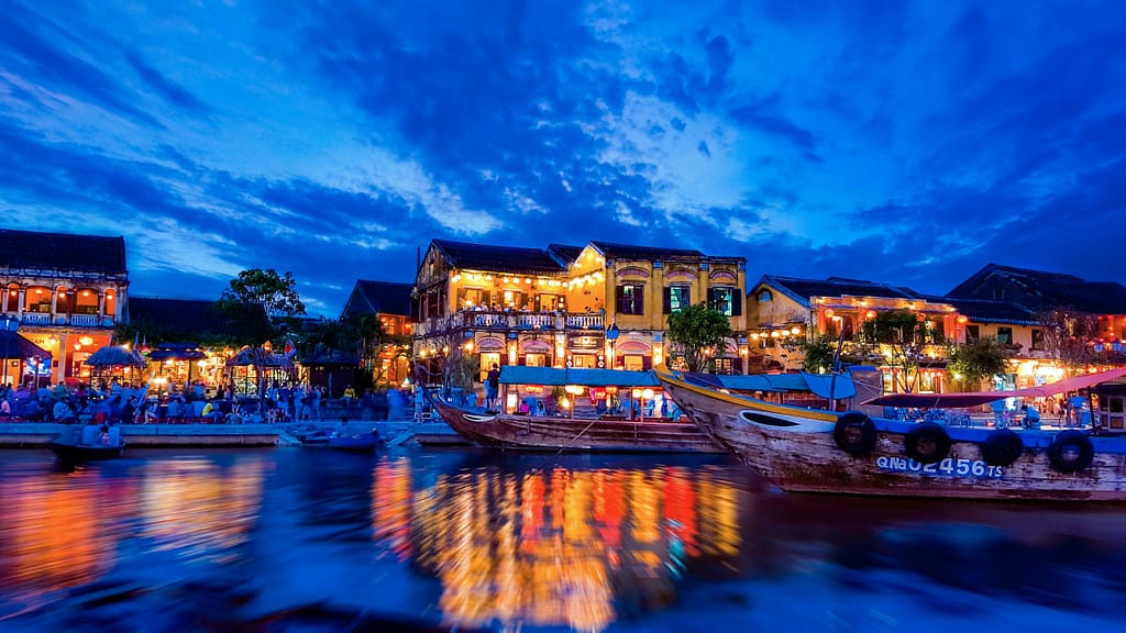 Enchanting view of Hội An's riverside with colorful lights reflecting on water at night.