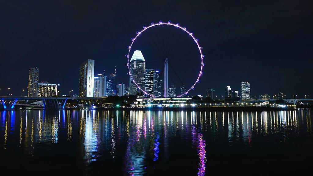 View of Singapore's skyline with the illuminated Singapore Flyer reflecting on Marina Bay at night.