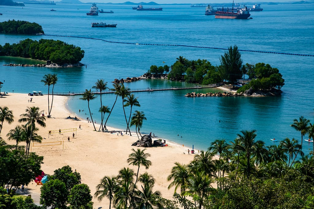 Stunning aerial view of a tropical beach with white sand and palm trees surrounded by blue waters and small islands.