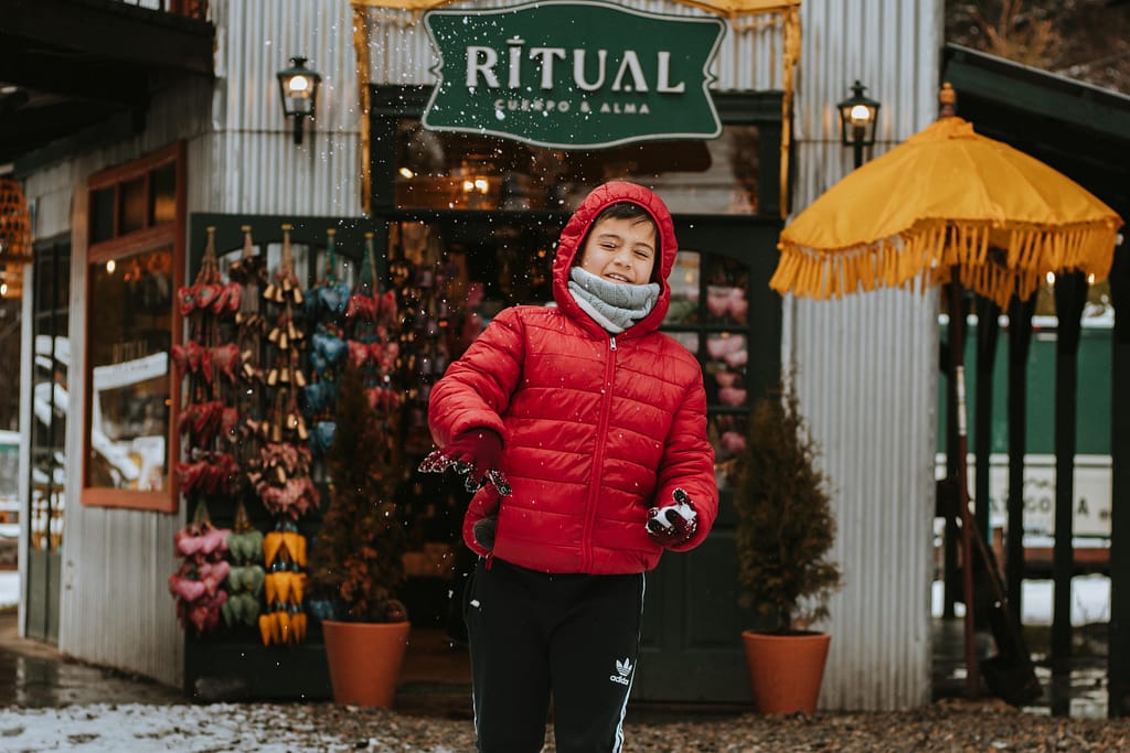 Boy in a red jacket plays with snow outside a shop in Colonia Suiza, Argentina.