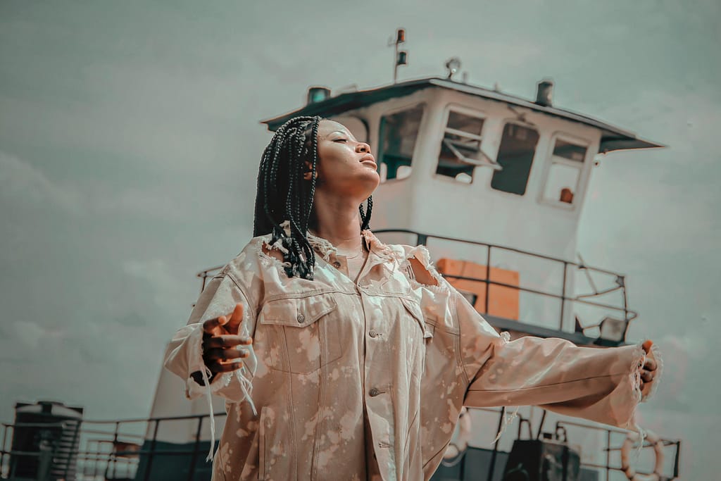 A joyful woman with braided hair poses in front of a ship, exuding happiness.