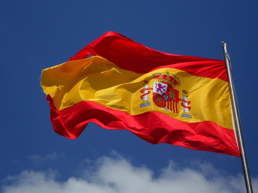 Vibrant Spanish flag waving against a clear blue sky and clouds.