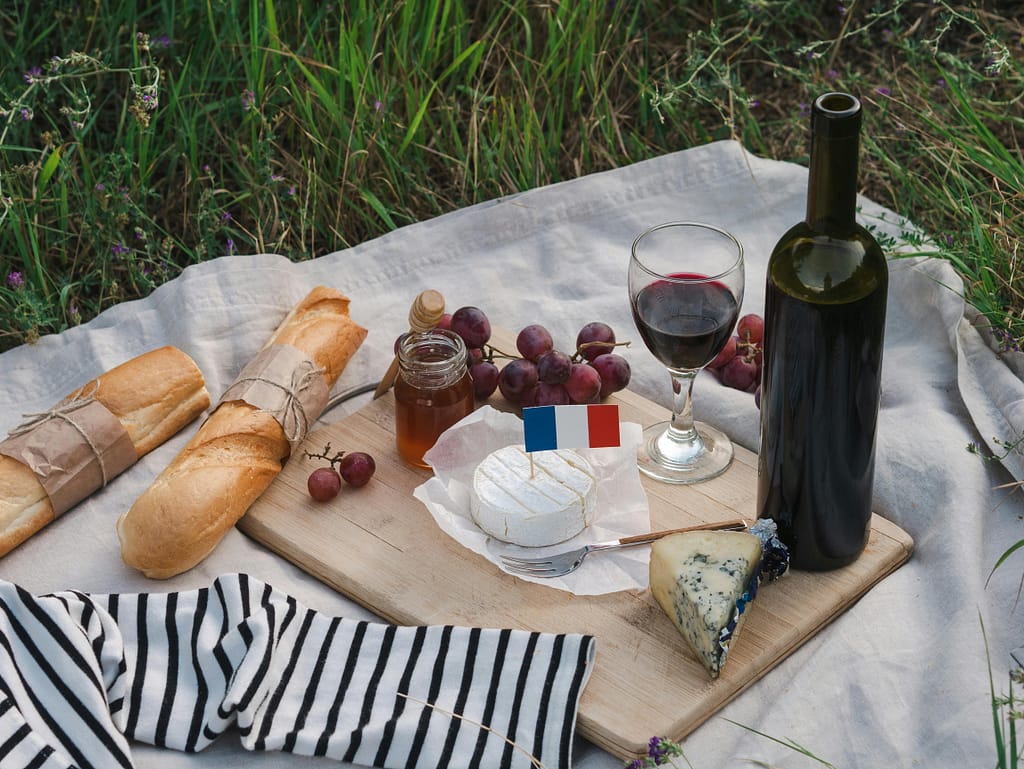 Charming French picnic setup with wine, cheese, baguette, and grapes on a wooden board outdoors.