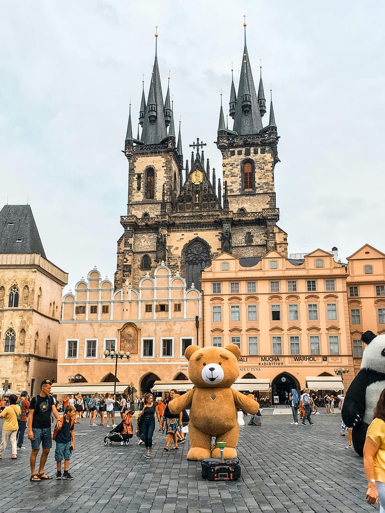 Visitors enjoying Prague's Old Town Square with St. Vitus Cathedral and playful mascots in the foreground.